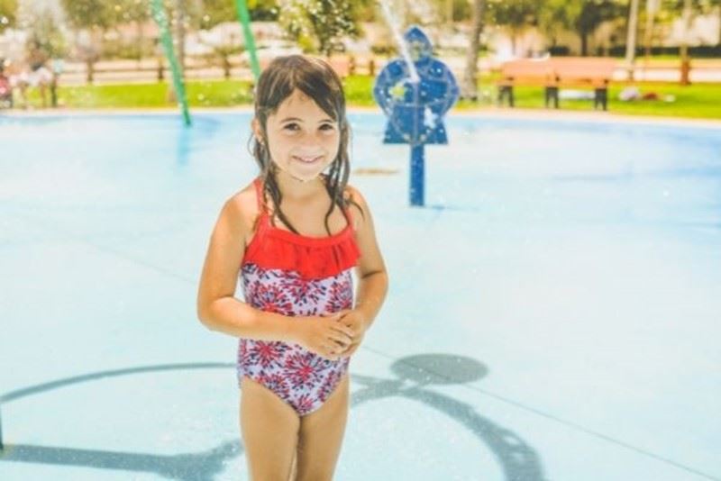 A girl standing on a splash pad with water jets behind her