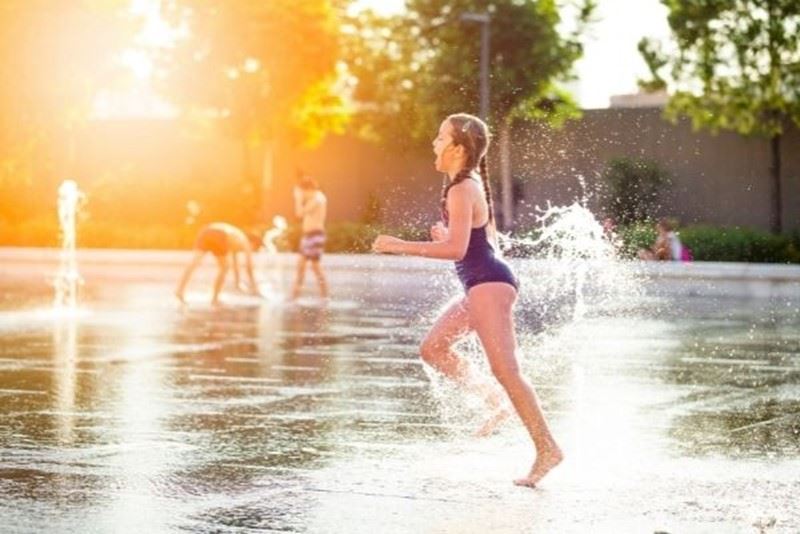 A girl running through the water at a splash pad in the evening sun