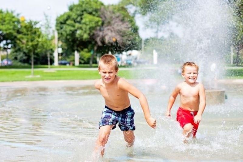 Two boys running through the spray at a splash pad